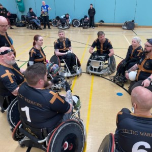 a group of people in wheelchairs is a circle. The people are wearing the celtic warriors team colours of black and gold